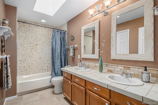 bathroom with toilet, a skylight, double vanity, and a sink