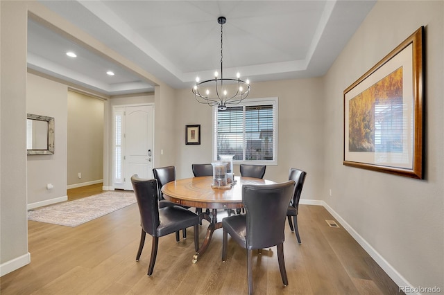 dining room featuring a tray ceiling, light hardwood / wood-style flooring, and a notable chandelier