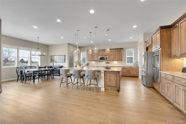 kitchen featuring a spacious island, a kitchen bar, light stone counters, appliances with stainless steel finishes, and pendant lighting