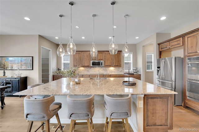 kitchen featuring hanging light fixtures, appliances with stainless steel finishes, a kitchen breakfast bar, a large island, and light stone countertops