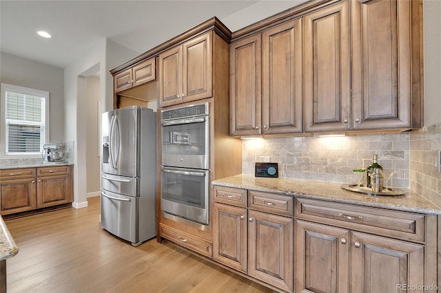 kitchen featuring light stone countertops, appliances with stainless steel finishes, light hardwood / wood-style floors, and decorative backsplash