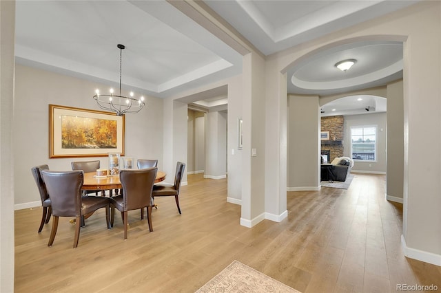 dining room with a stone fireplace, light hardwood / wood-style flooring, a notable chandelier, and a tray ceiling