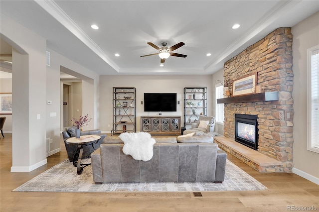 living room featuring a raised ceiling, ornamental molding, a stone fireplace, and light hardwood / wood-style floors