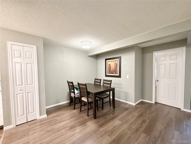 dining room featuring baseboards, a textured ceiling, and wood finished floors
