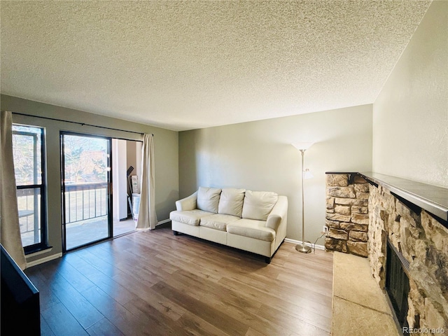 living area with a fireplace, a textured ceiling, baseboards, and wood finished floors
