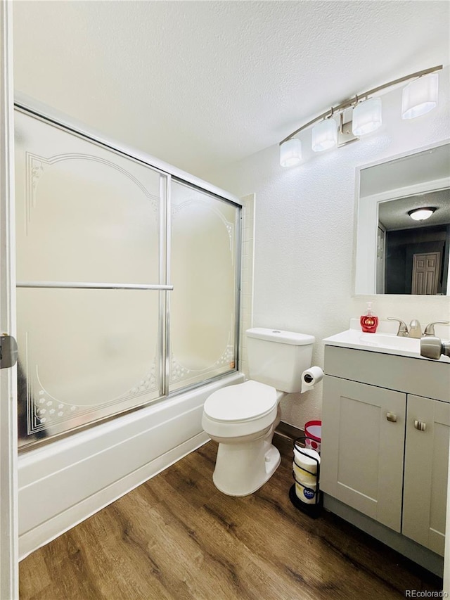 full bath featuring a textured ceiling, vanity, toilet, wood finished floors, and bath / shower combo with glass door
