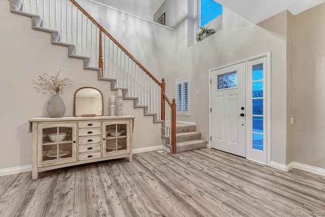 foyer with baseboards, wood finished floors, stairway, and a towering ceiling
