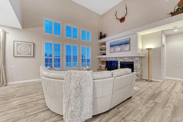 living room with a high ceiling, baseboards, light wood finished floors, and a fireplace