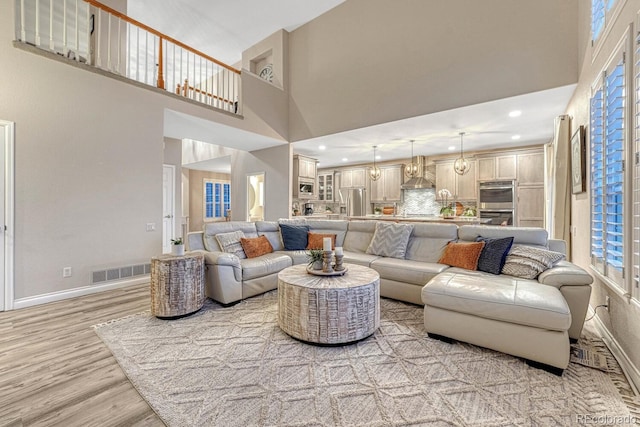 living room featuring light wood-type flooring, baseboards, a high ceiling, and visible vents