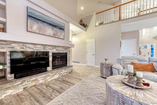living room featuring visible vents, a towering ceiling, wood finished floors, a fireplace, and baseboards
