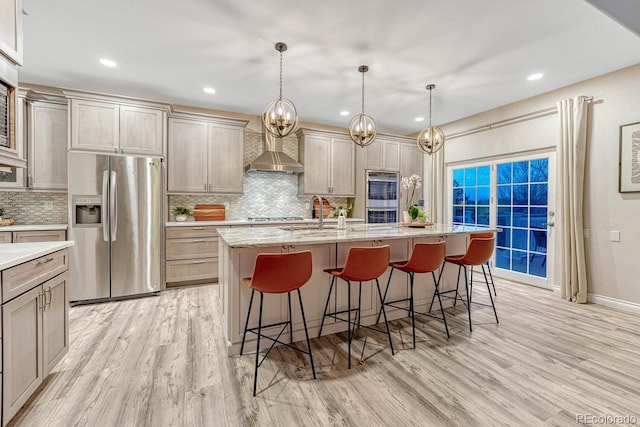 kitchen featuring light wood-style flooring, appliances with stainless steel finishes, wall chimney range hood, and tasteful backsplash