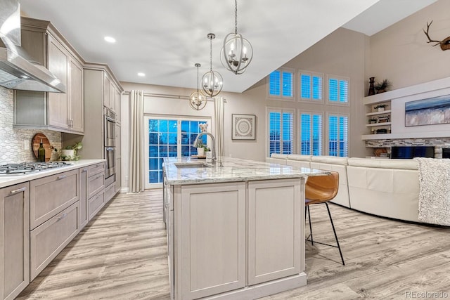 kitchen featuring wall chimney range hood, gray cabinets, a sink, stainless steel appliances, and light wood-style flooring