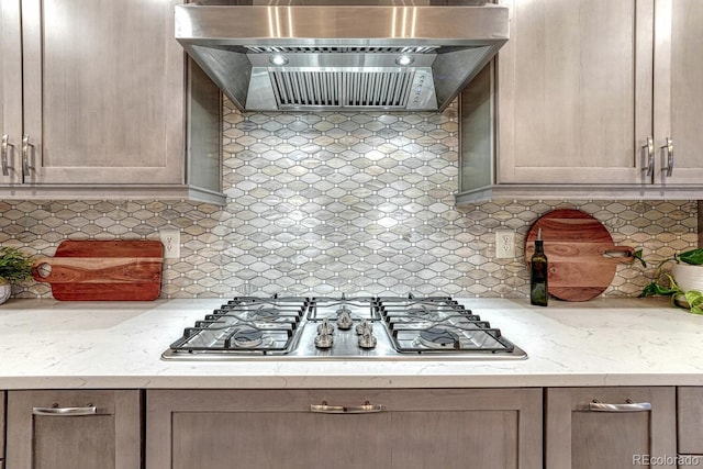 kitchen with decorative backsplash, wall chimney exhaust hood, stainless steel gas cooktop, and light stone countertops