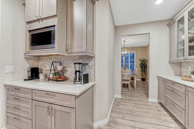 bar featuring an inviting chandelier, baseboards, stainless steel microwave, tasteful backsplash, and light wood-style flooring