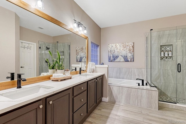 bathroom featuring a sink, double vanity, a shower stall, wood finished floors, and a bath
