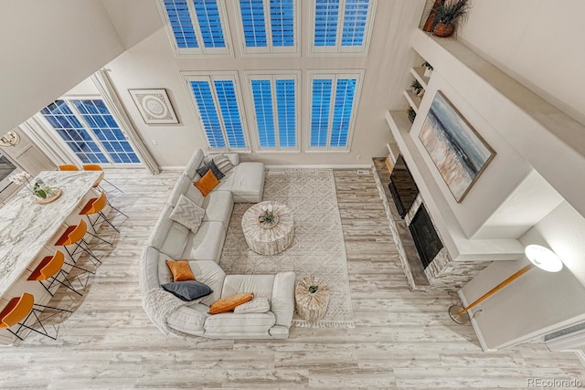 living room featuring a fireplace with flush hearth, wood finished floors, and a towering ceiling