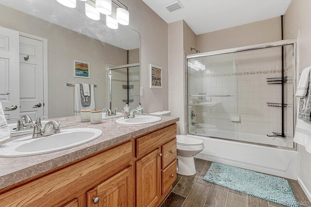 bathroom with visible vents, a sink, bath / shower combo with glass door, and wood finished floors