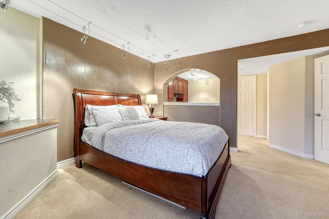 bedroom with baseboards, light carpet, and arched walkways
