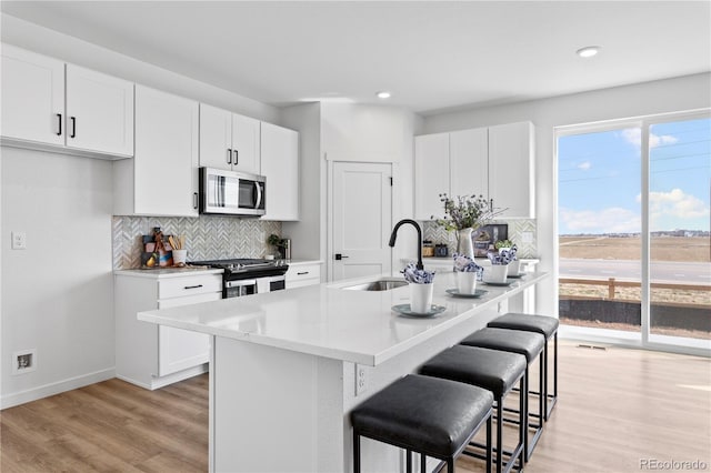 kitchen featuring appliances with stainless steel finishes, a sink, a breakfast bar area, backsplash, and white cabinetry