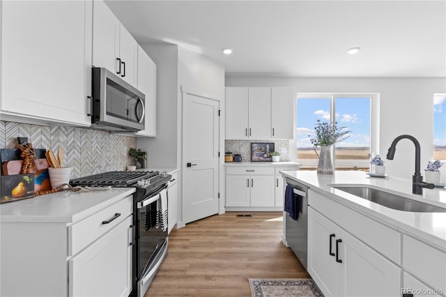 kitchen featuring stainless steel appliances, a sink, light countertops, light wood-style flooring, and recessed lighting