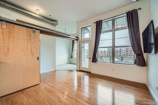empty room with a barn door, plenty of natural light, and wood finished floors