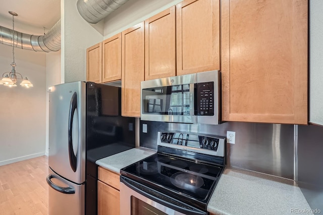 kitchen with light brown cabinets, light wood-style flooring, an inviting chandelier, light countertops, and appliances with stainless steel finishes
