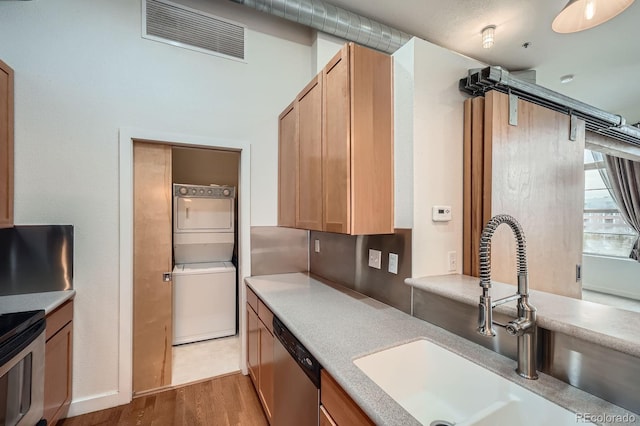 kitchen featuring wood finished floors, a sink, stacked washing maching and dryer, stainless steel appliances, and visible vents