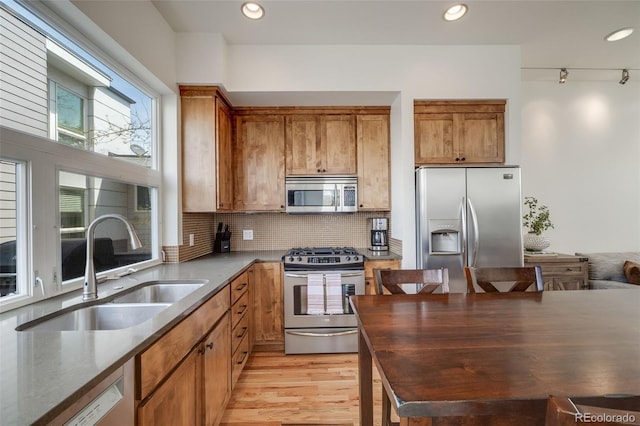 kitchen featuring brown cabinetry, a sink, decorative backsplash, and appliances with stainless steel finishes