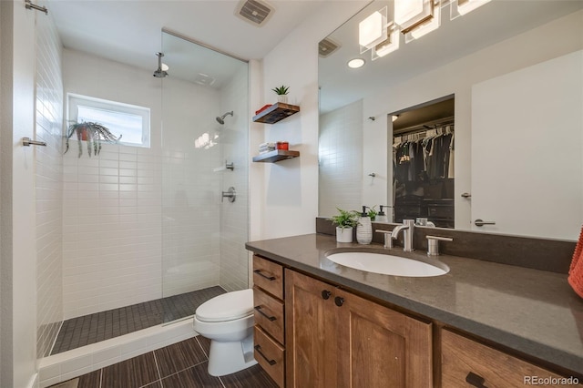 full bath featuring vanity, toilet, tiled shower, and visible vents