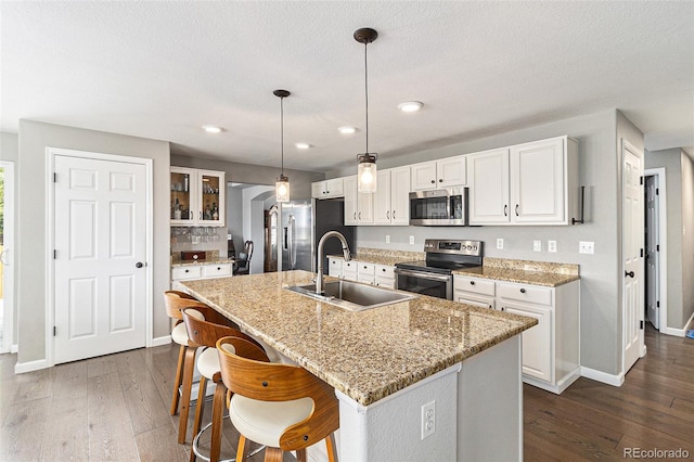 kitchen featuring sink, white cabinetry, stainless steel appliances, a center island with sink, and decorative light fixtures