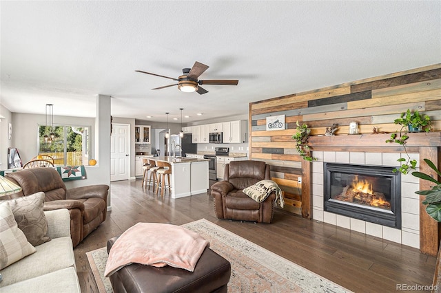 living room with sink, a textured ceiling, dark hardwood / wood-style floors, a tile fireplace, and ceiling fan