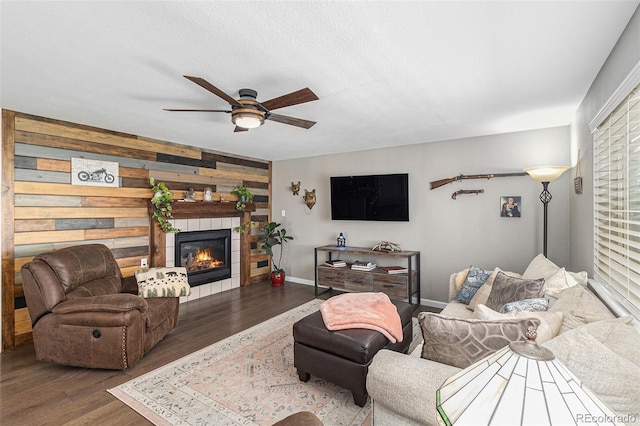 living room with a fireplace, dark wood-type flooring, ceiling fan, and wood walls