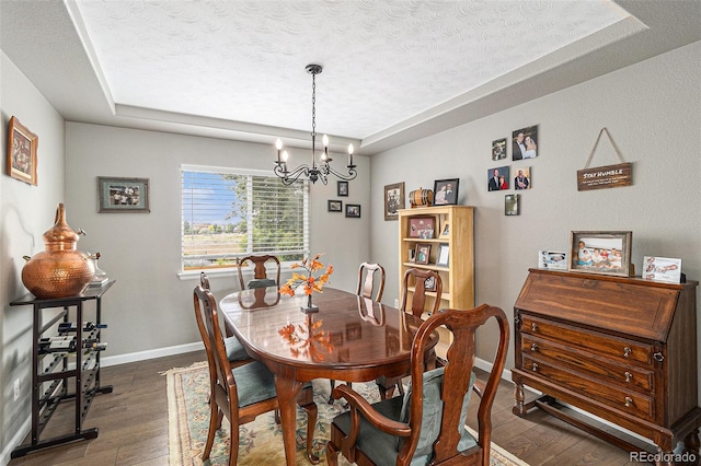 dining space featuring dark wood-type flooring, a notable chandelier, a textured ceiling, and a tray ceiling