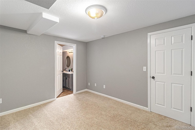 unfurnished bedroom with ensuite bathroom, a textured ceiling, and carpet