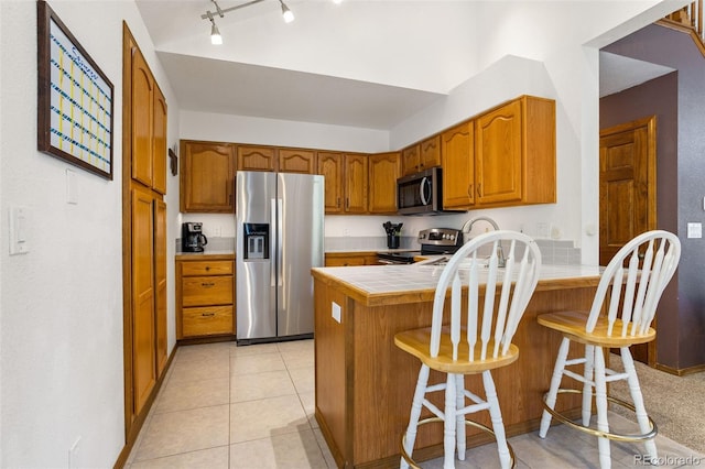 kitchen with a breakfast bar, appliances with stainless steel finishes, tile counters, light tile patterned flooring, and kitchen peninsula