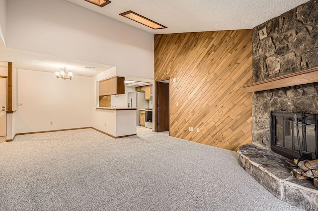 unfurnished living room with wooden walls, high vaulted ceiling, a stone fireplace, and light colored carpet