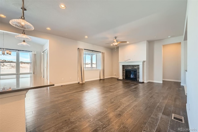 unfurnished living room with ceiling fan with notable chandelier, dark hardwood / wood-style floors, and a stone fireplace