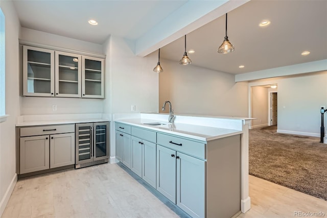 kitchen featuring kitchen peninsula, wine cooler, sink, decorative light fixtures, and light colored carpet