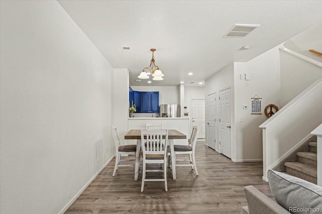 dining space featuring light wood-type flooring, visible vents, a notable chandelier, and stairs