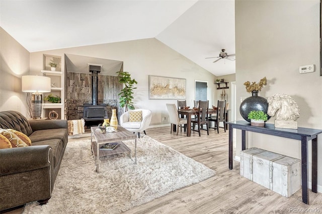 living area with a wood stove, a ceiling fan, baseboards, wood finished floors, and lofted ceiling