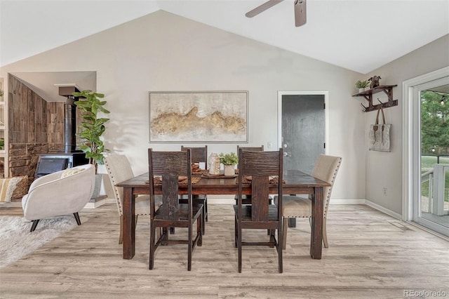 dining space featuring a ceiling fan, lofted ceiling, light wood-style flooring, and a wood stove