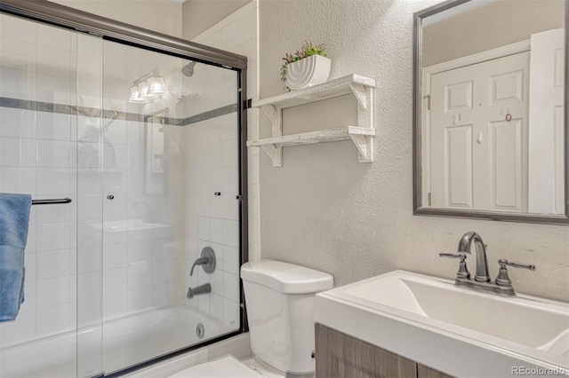 bathroom with enclosed tub / shower combo, a textured wall, toilet, and vanity