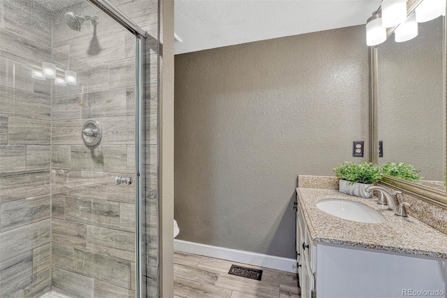 bathroom with visible vents, vanity, wood finished floors, toilet, and a stall shower