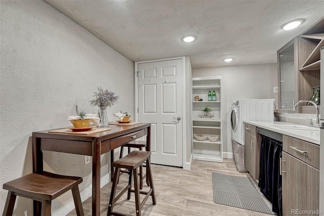 clothes washing area with laundry area, a textured wall, light wood-type flooring, a textured ceiling, and a sink