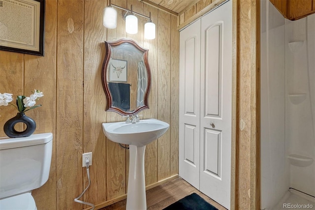 bathroom with wooden walls, toilet, and wood finished floors