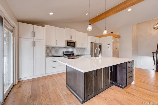 kitchen with a sink, vaulted ceiling with beams, light wood finished floors, and stainless steel appliances