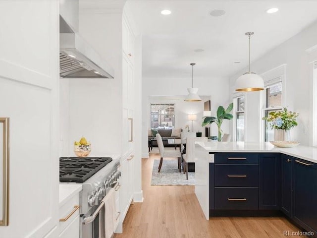 kitchen with a healthy amount of sunlight, stainless steel stove, light countertops, and wall chimney range hood