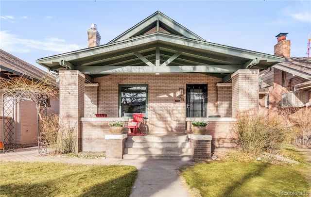 view of exterior entry featuring central air condition unit, covered porch, brick siding, and a chimney