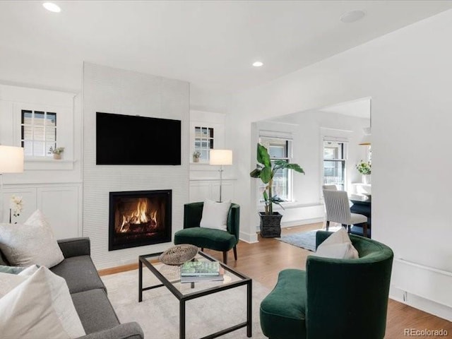 living room with recessed lighting, baseboards, a lit fireplace, and wood finished floors