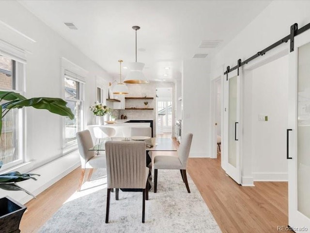 dining room featuring a barn door, light wood-style floors, visible vents, and baseboards